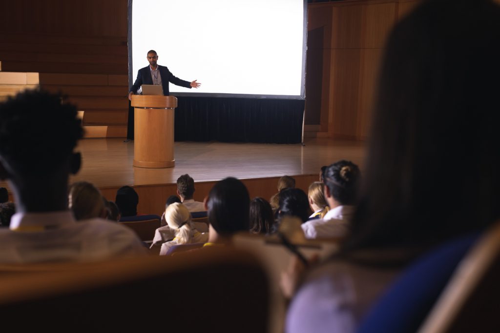 View from the audience perspective of presenter speaking in a large conference hall